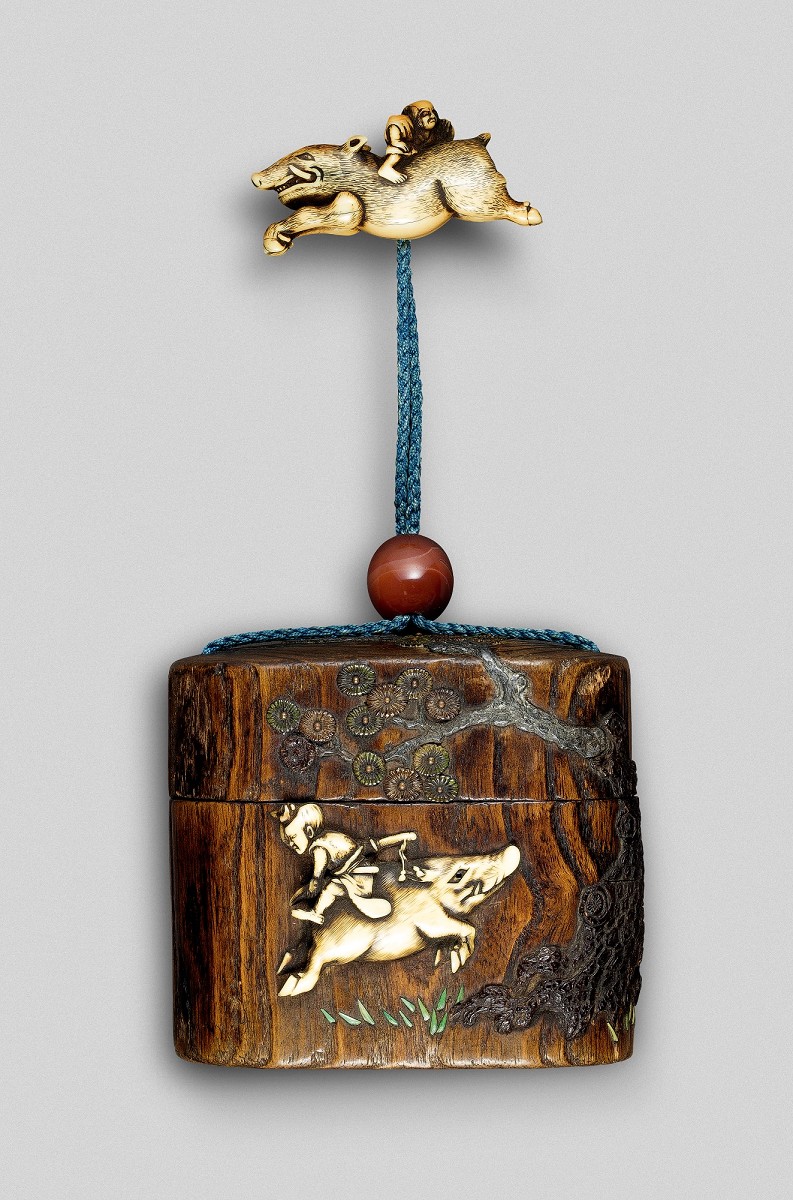 Ein Vasall reitet rückwärts auf einem galoppierenden Eber. Gleiches Motiv auf Tonkotsu, Kiri-Holz mit Elfenbein-Relief und Netsuke aus Elfenbein. Japan, Edo-Zeit (1602–1868). Foto: Jean Marie Colrat, St. Gratien
